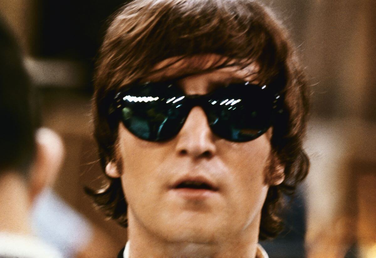 John Lennon wears a pair of oversized sunglasses.