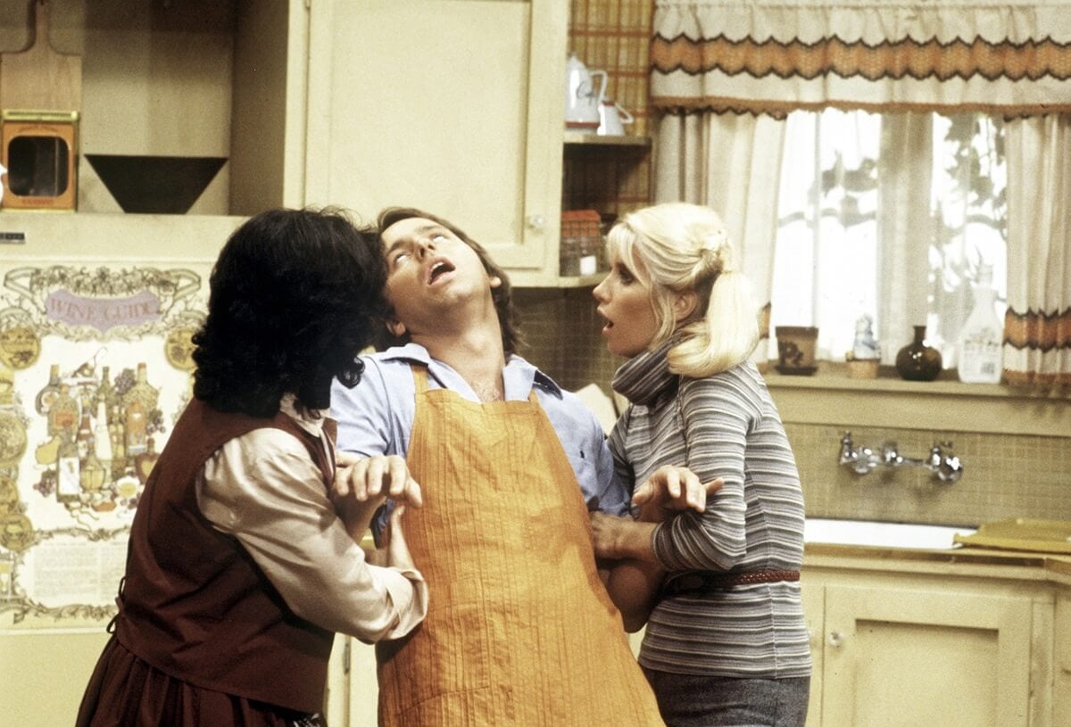 A scene from 'Three's Company' where John Ritter's Jack Jack (John Ritter) feigns an illness for Janet (Joyce DeWitt) and Chrissy (Suzanne Somers).