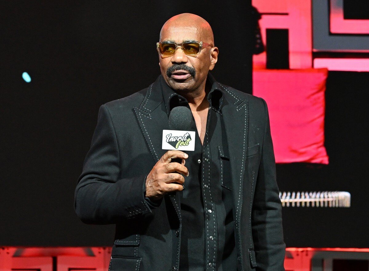 Steve Harvey speaking onstage during Day 2 of 2023 Invest Fest at Georgia World Congress Center in a black suit.