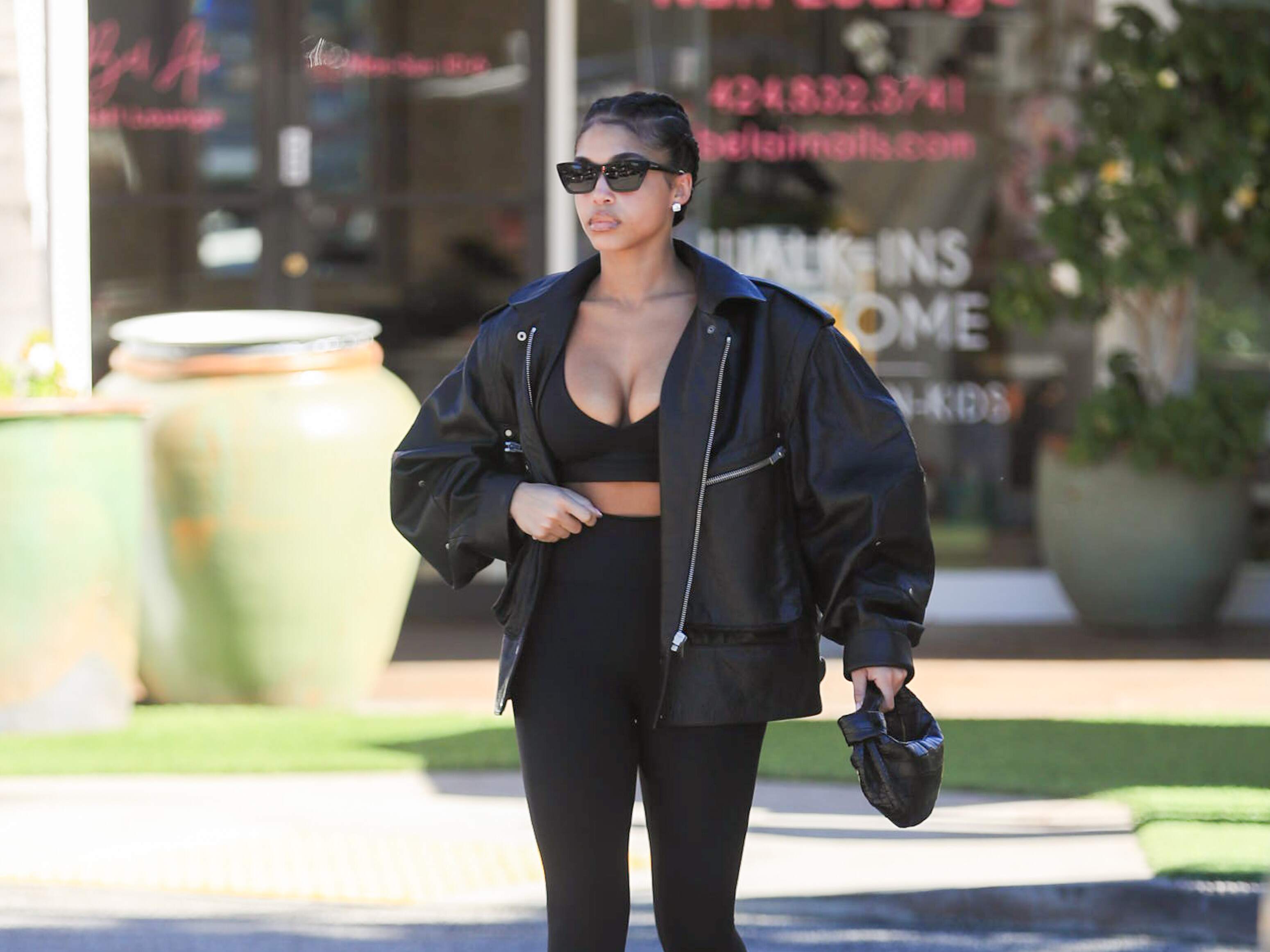 Model Lori Harvey picks up an iced coffee on a sunny day in LA while wearing a leather jacket and black leggings