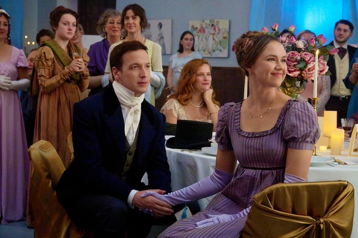 A man in a suit sitting next to a woman in a purple empire-waist dress