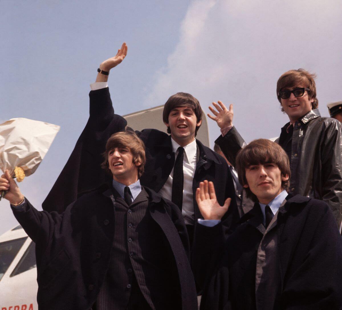 Ringo Starr, Paul McCartney, George Harrison, and John Lennon of The Beatles wave from the open door of an airplane.