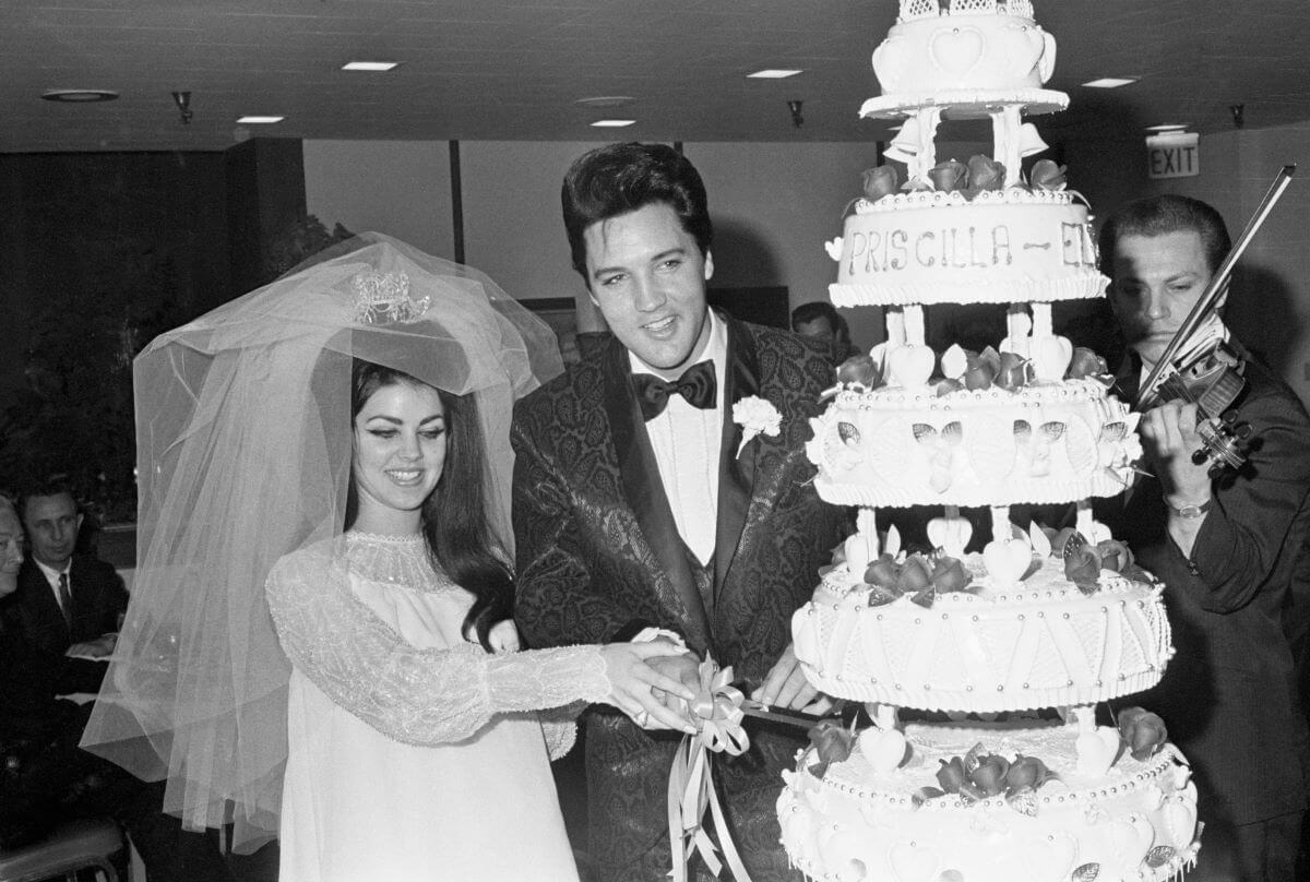 A black and white picture of Priscilla and Elvis Presley cutting their wedding cake.