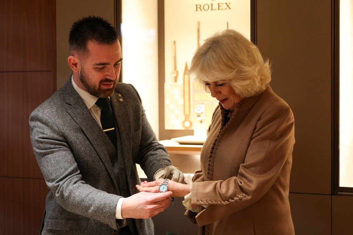 Man helping Queen Camilla try on a wristwatch