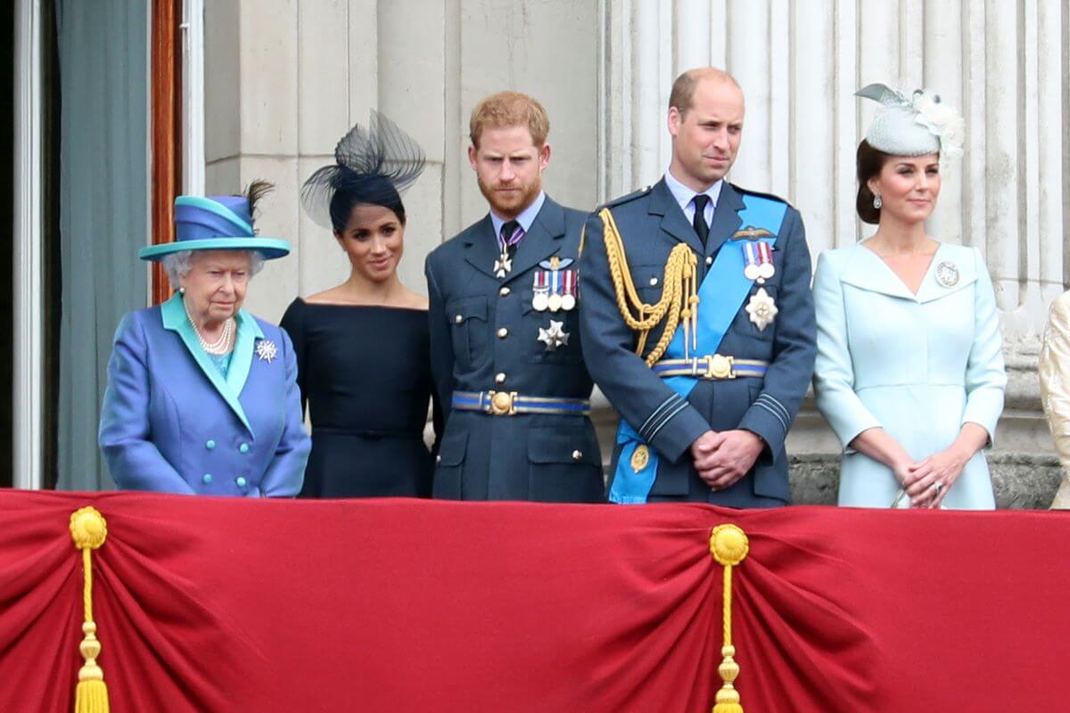 Queen Elizabeth II, Meghan Markle, Prince Harry, Prince William, and Kate Middleton standing on the balcony of Buckingham Palace during a flypast