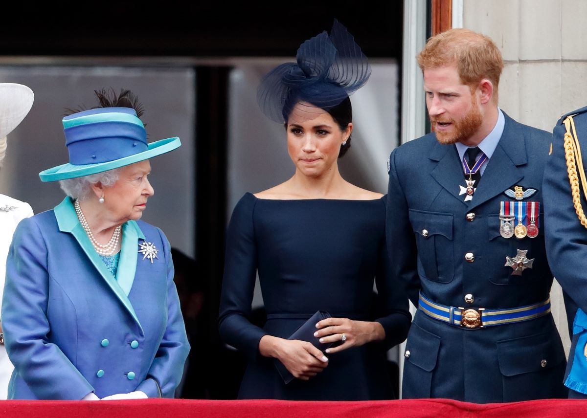 Queen Elizabeth II, Meghan Markle, and Prince Harry standing on the balcony of Buckingham Palace for a flypast
