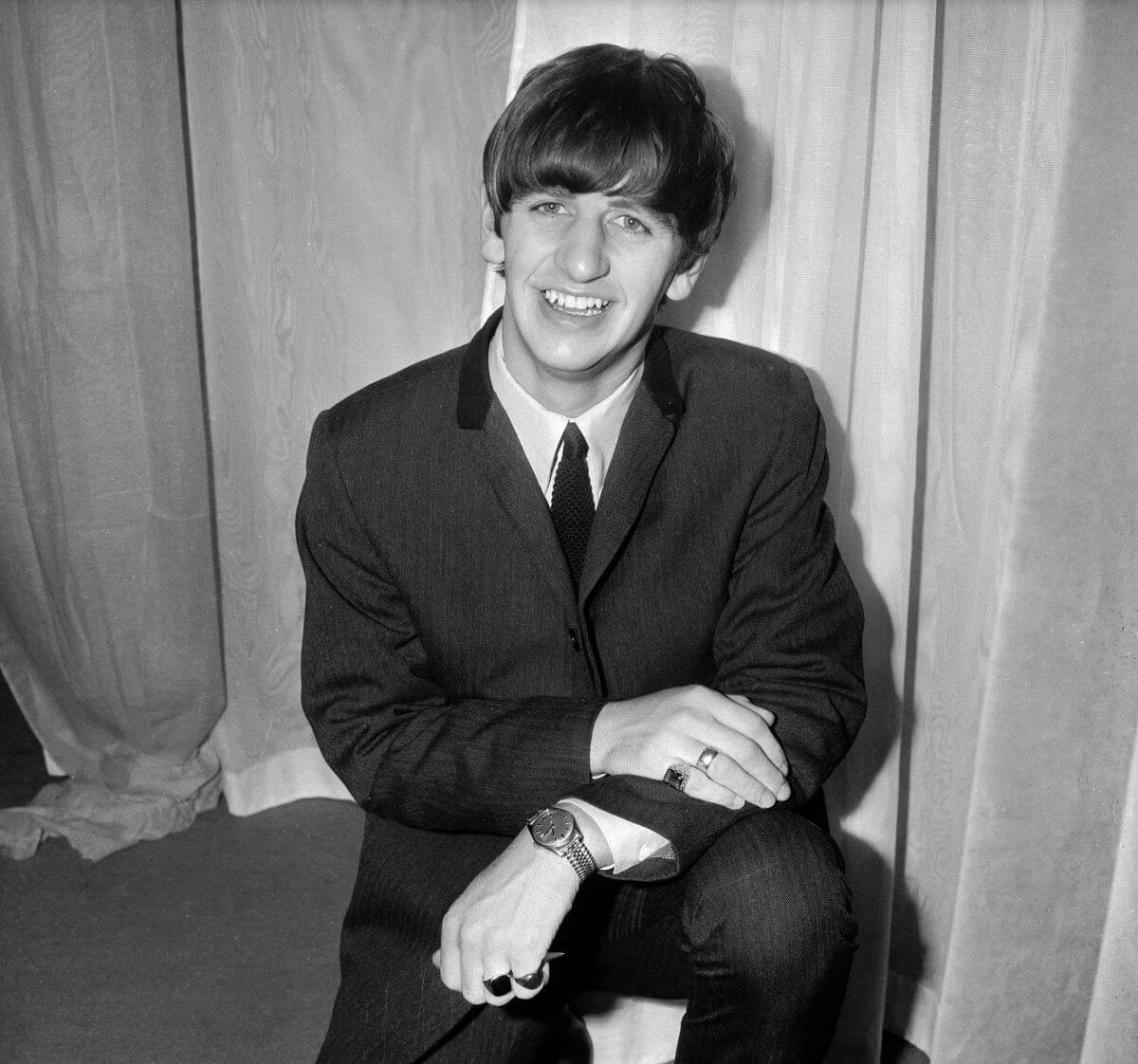 A black and white picture of Ringo Starr wearing a suit and kneeling.