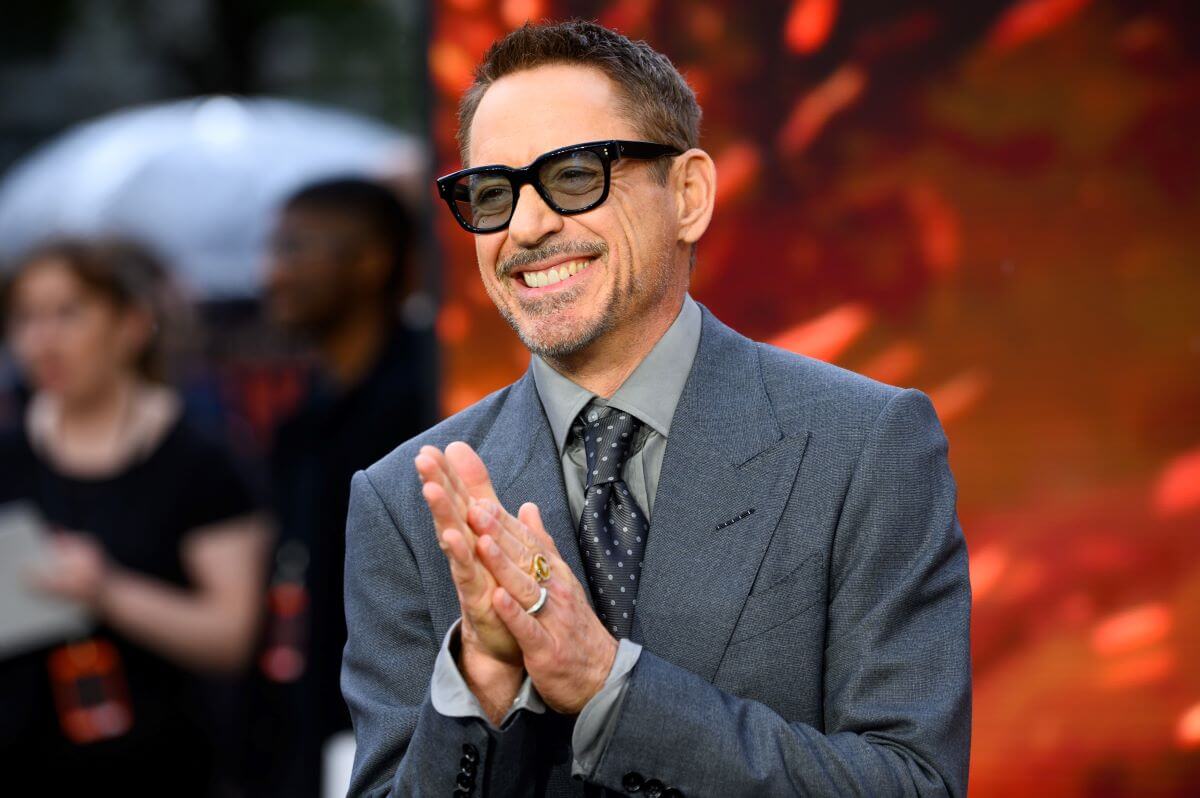 Robert Downey Jr. wears a suit and sunglasses at the premiere of 'Oppenheimer.' He presses his palms together.