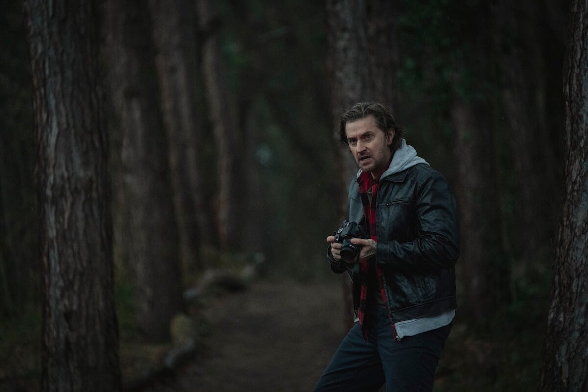Richard Armitage holding a camera and standing in the trees in 'Stay Close'