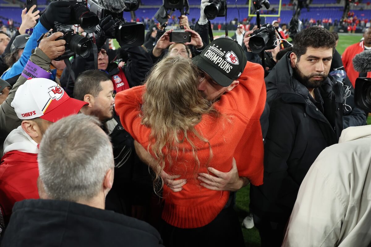 Taylor Swift and Travis Kelce embrace while surrounded by crowd of people