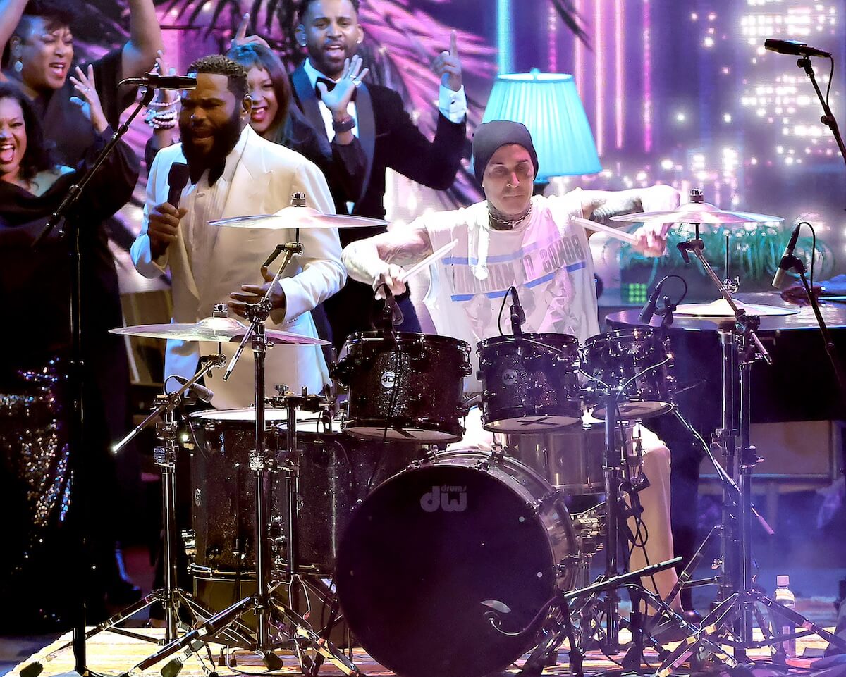 Anthony Anderson, in white jacket, stands next to drumming Travis Barker at the 75th Emmy Awards