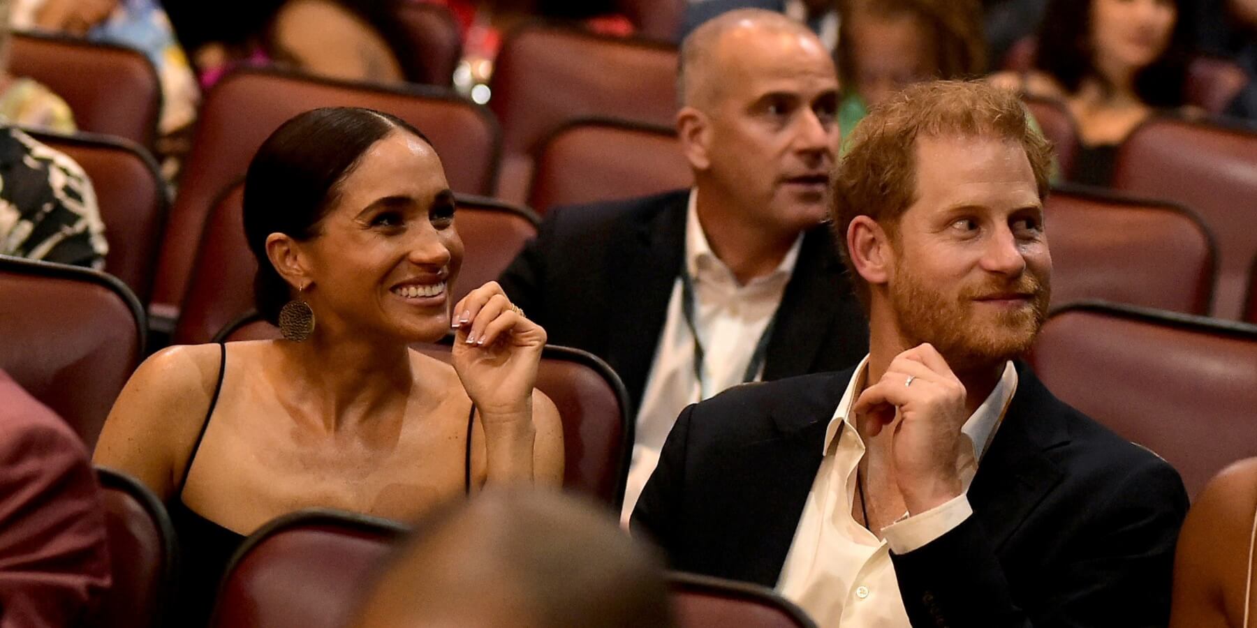 Meghan Markle and Prince Harry smile while seated in a theater.