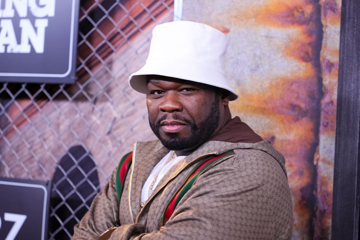 50 Cent posing at the premiere of "Power Book III: Raising Kanan" in a brown jacket and white hat.