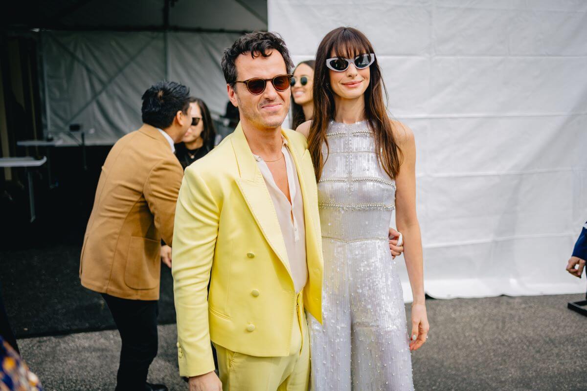 Andrew Scott wears a yellow suit and sunglasses and has his arm around Anne Hathaway's waist.