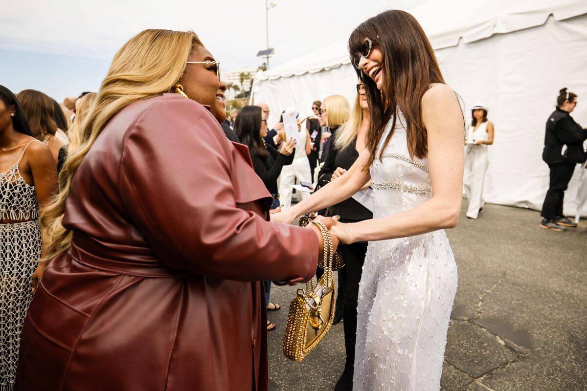 Da'Vine Joy Randolph and Anne Hathaway hold hands at the Independent Spirit Awards. Randolph wears a leather jacket and Hathaway wears a silver pantsuit.