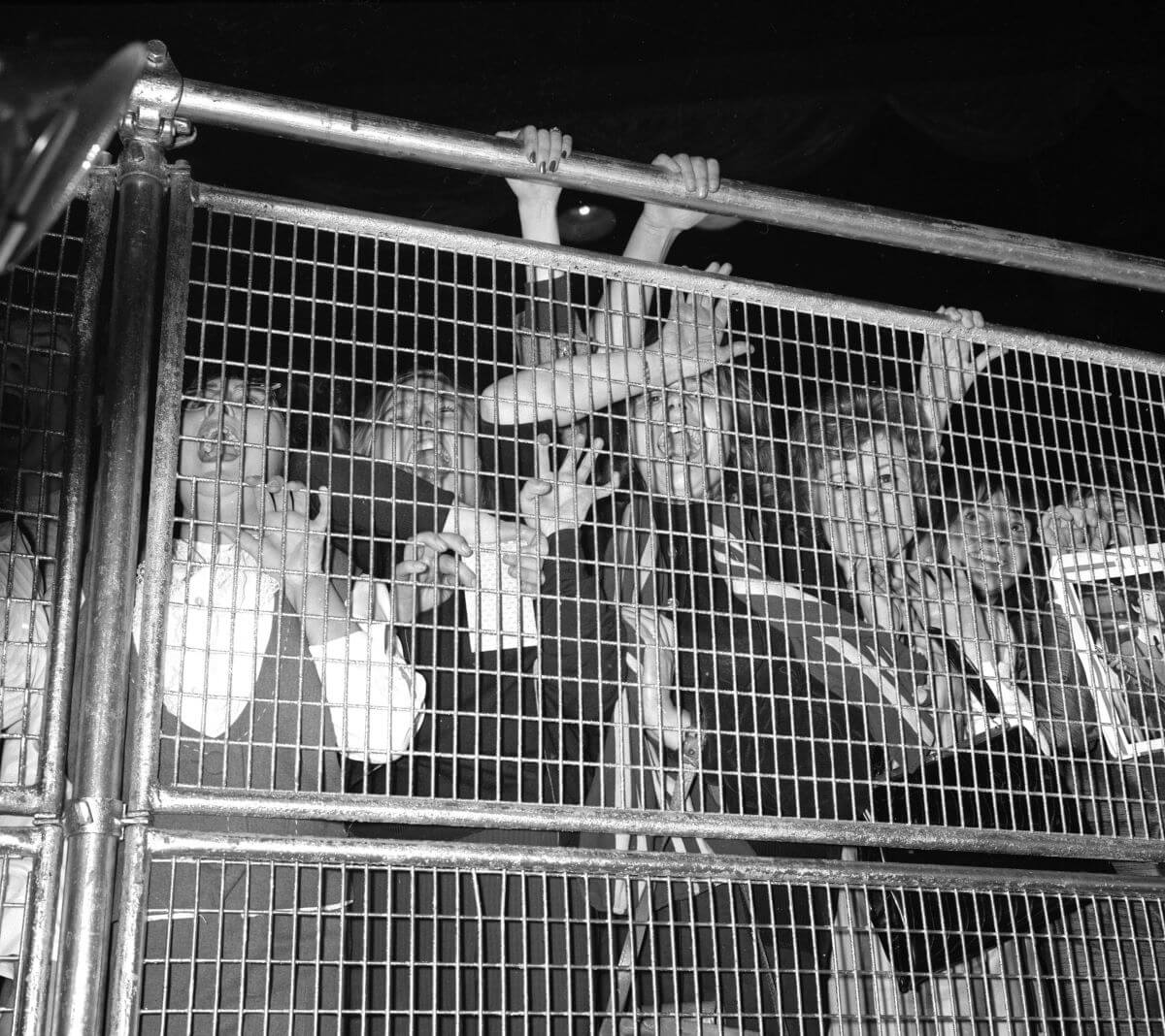 A black and white picture of Beatles fans pressing against a gate during a concert.