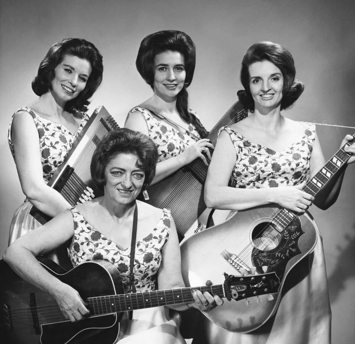 A black and white picture of June, Anita, Helen, and Maybelle Carter (seated). They each hold instruments and wear matching dresses. 