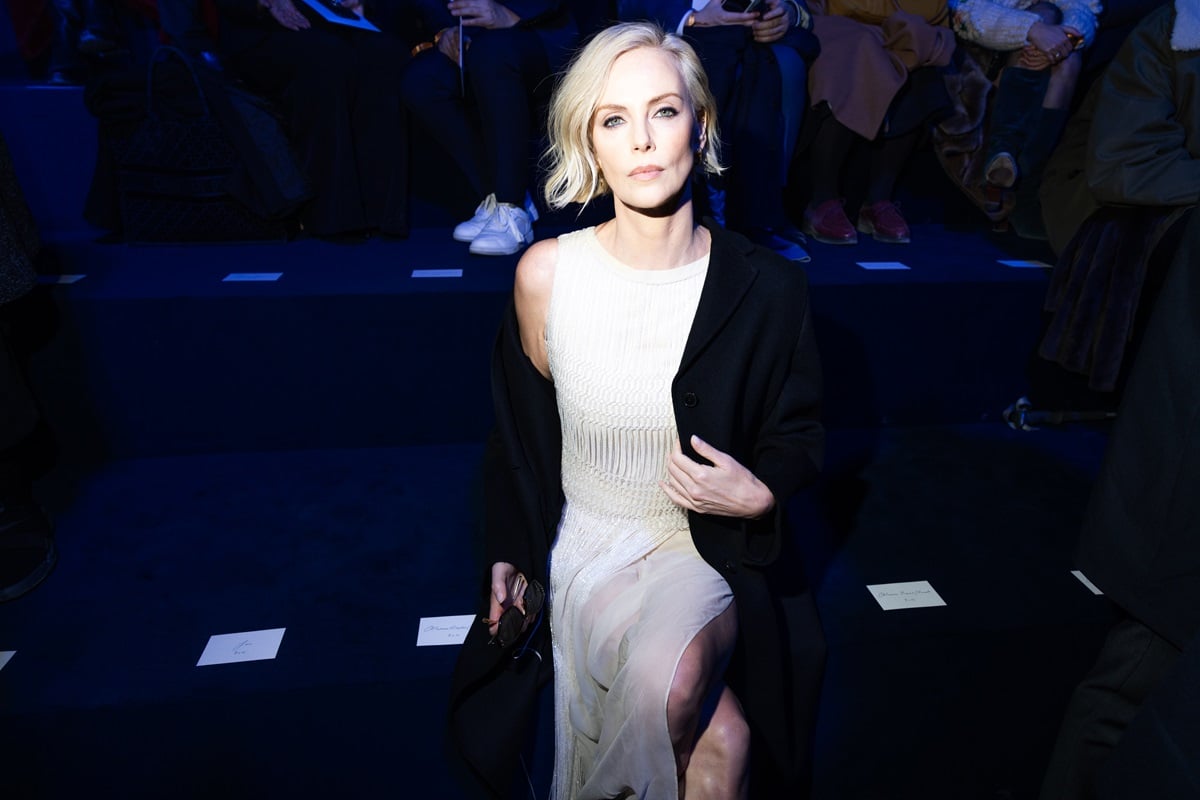 Charlize Theron posing in a black jacket and white dress at the the Christian Dior Womenswear Fall Winter 2023-2024 show.