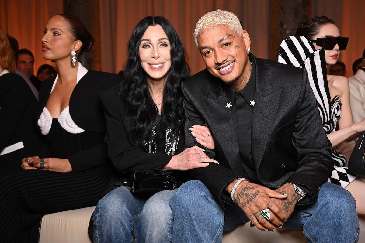 Singer Cher and Alexander Edwards smile together while sitting in the front row for the Balmain Womenswear Fall/Winter 2024-2025 show