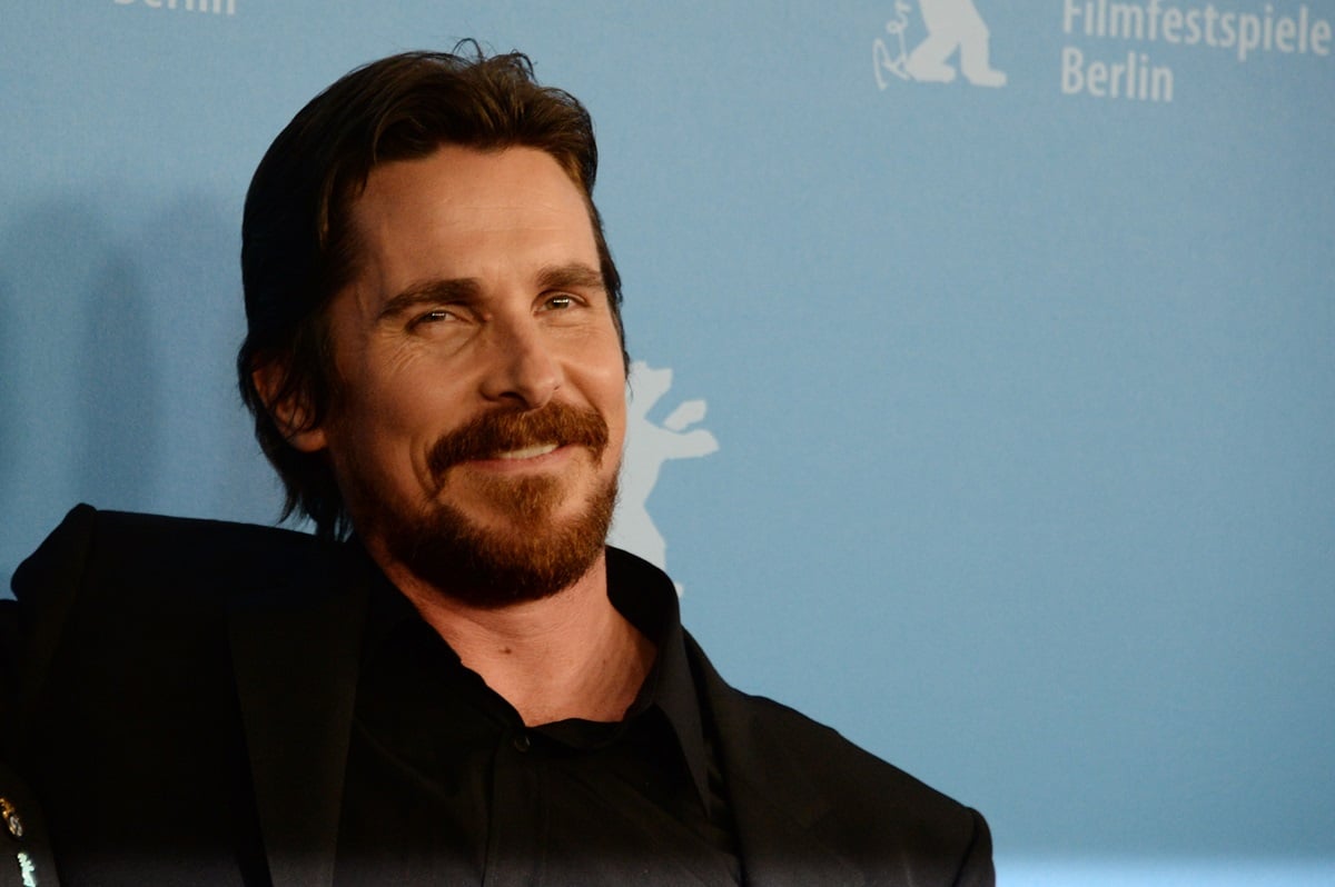 Christian Bale smirking while wearing a black suit at the 'American Hustle' photocall.