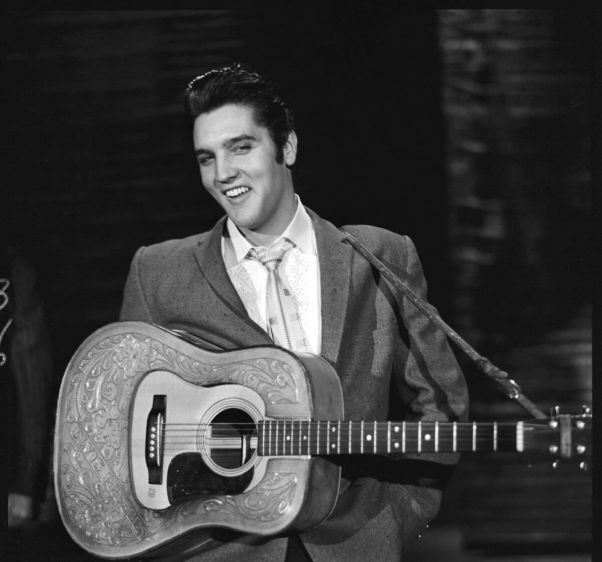 A black and white picture of Elvis Presley holding an acoustic guitar.
