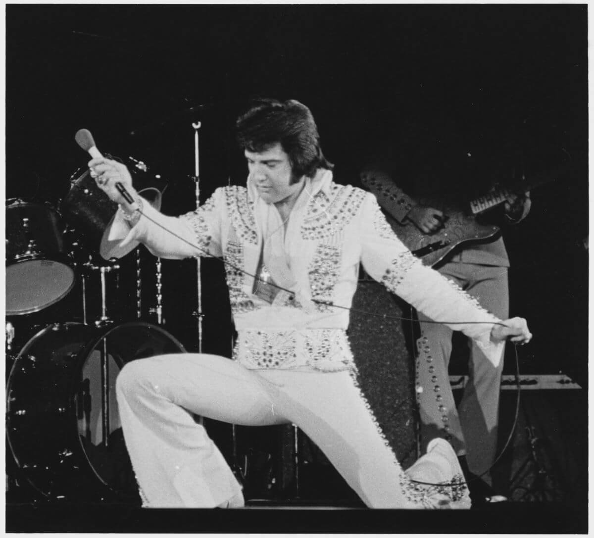 A black and white picture of Elvis kneeling during a concert and holding a microphone.