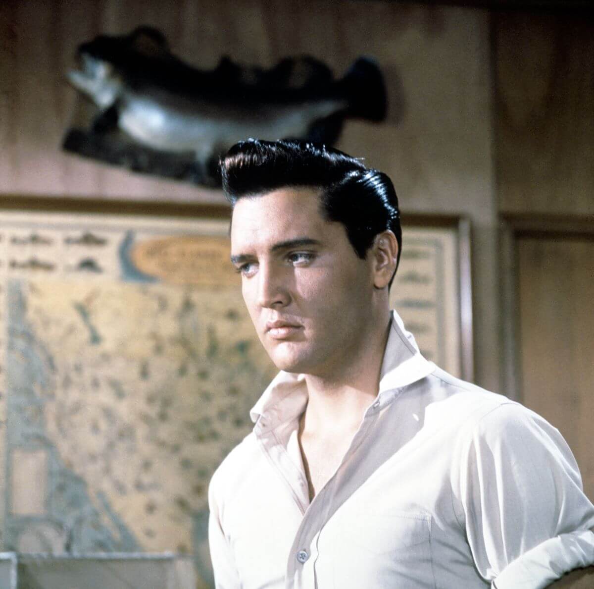 Elvis Presley wears a white shirt and stands in front of a map in the film 'Girls! Girls! Girls!'