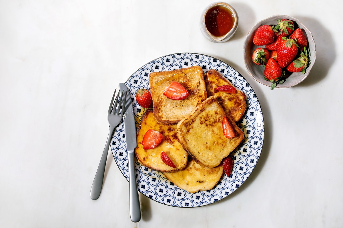 Pile of french toasts with fresh strawberries on ceramic plate. with maple syrup in ceramic jug. Travis Kelce eats the meal before ever game