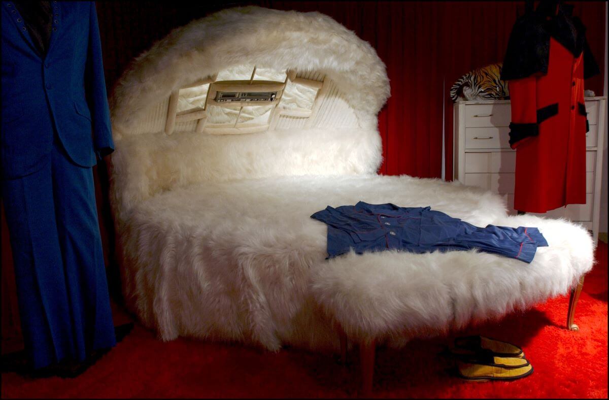 A white, fur covered bed at Graceland. The bedroom has red carpeting.