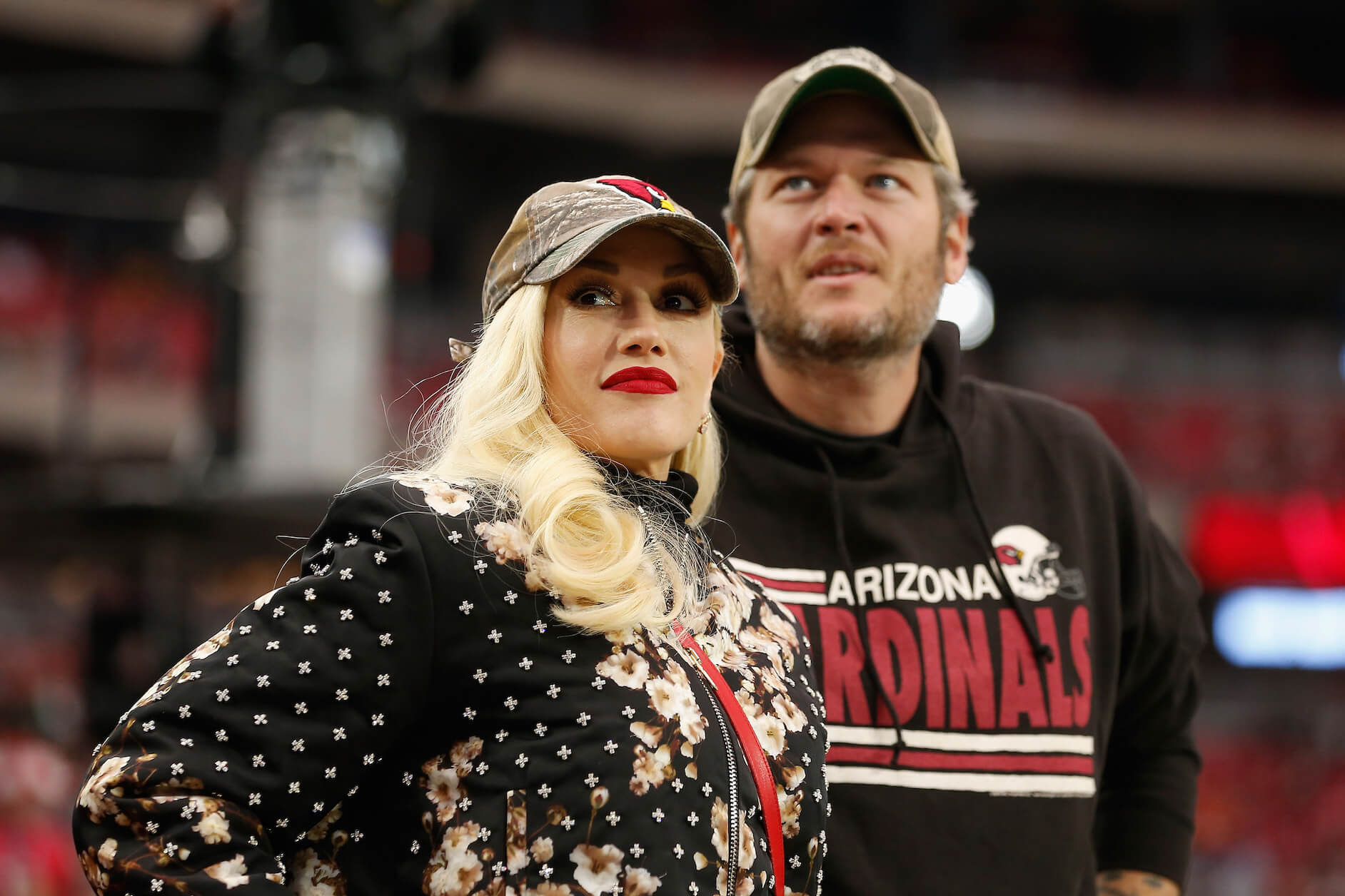 Blake Shelton wearing a Cardinals jersey and standing behind Gwen Stefani as they attend the NFL game between the Green Bay Packers and Arizona Cardinals