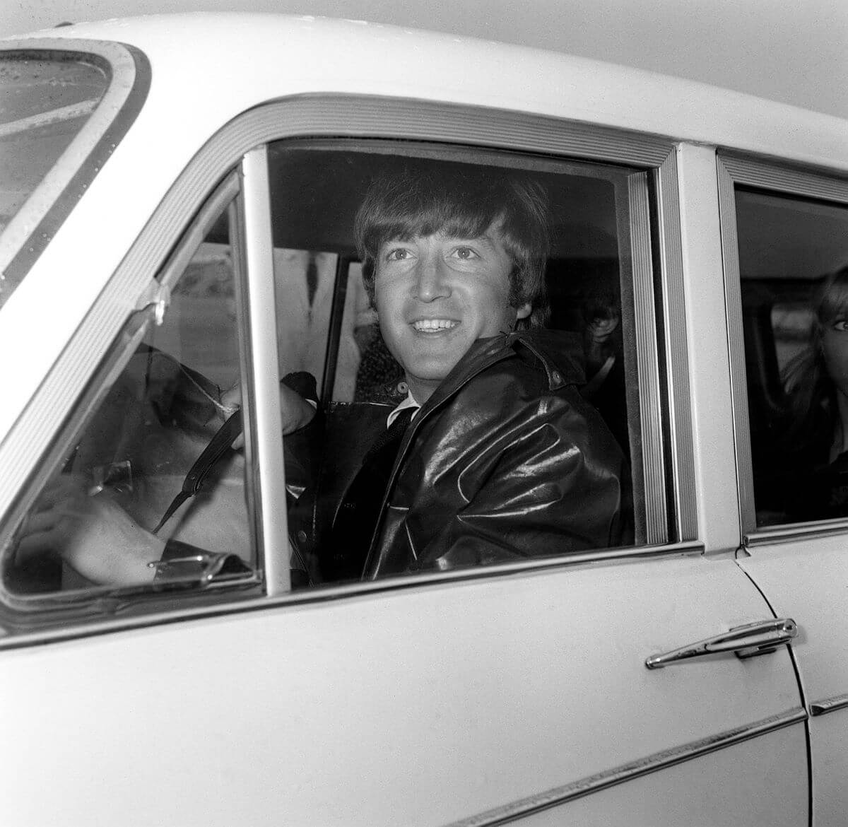 A black and white picture of John Lennon driving a car.