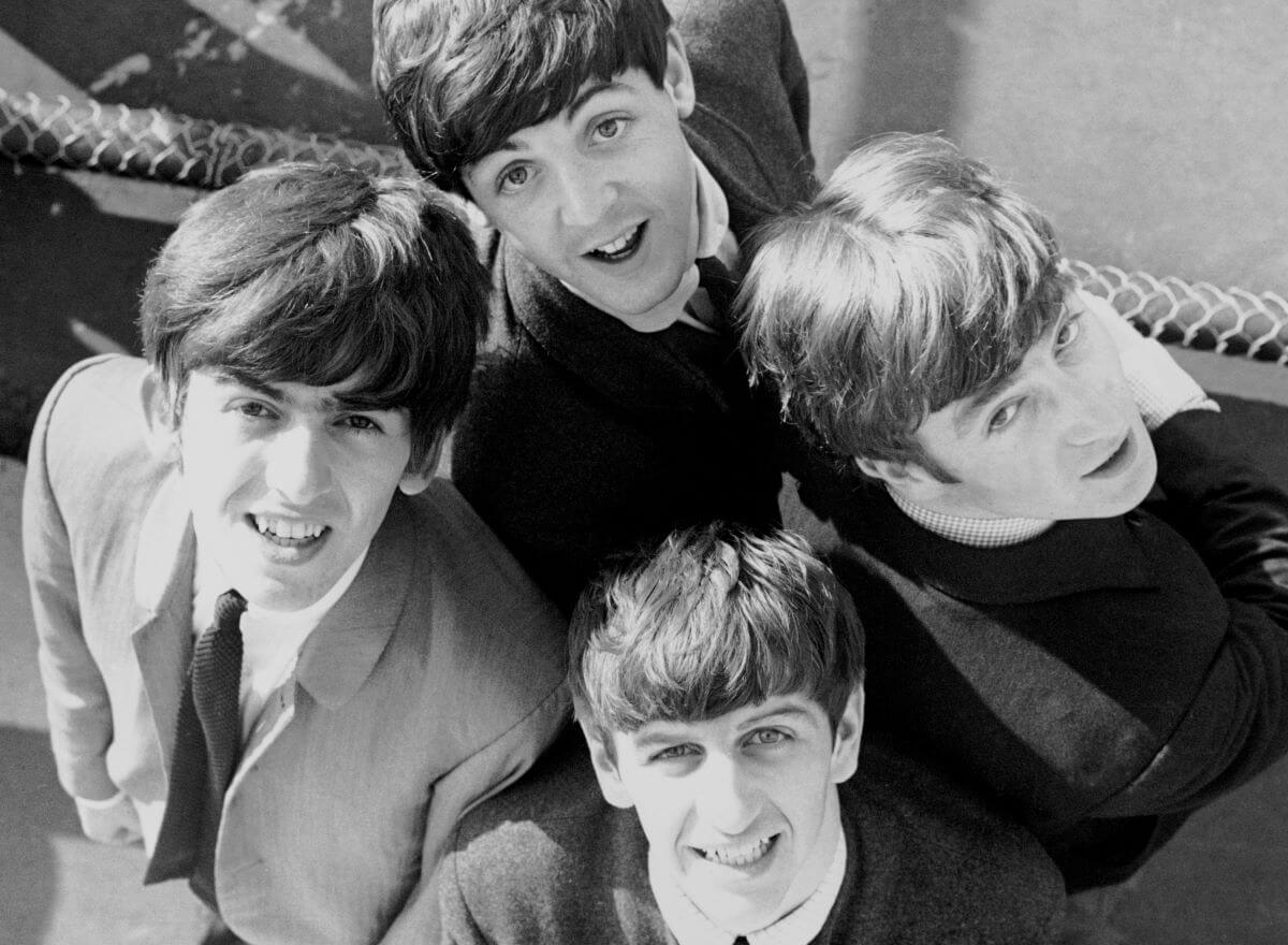 A black and white picture of George Harrison, Paul McCartney, John Lennon, and Ringo Starr of The Beatles wearing suits and looking up at the camera.