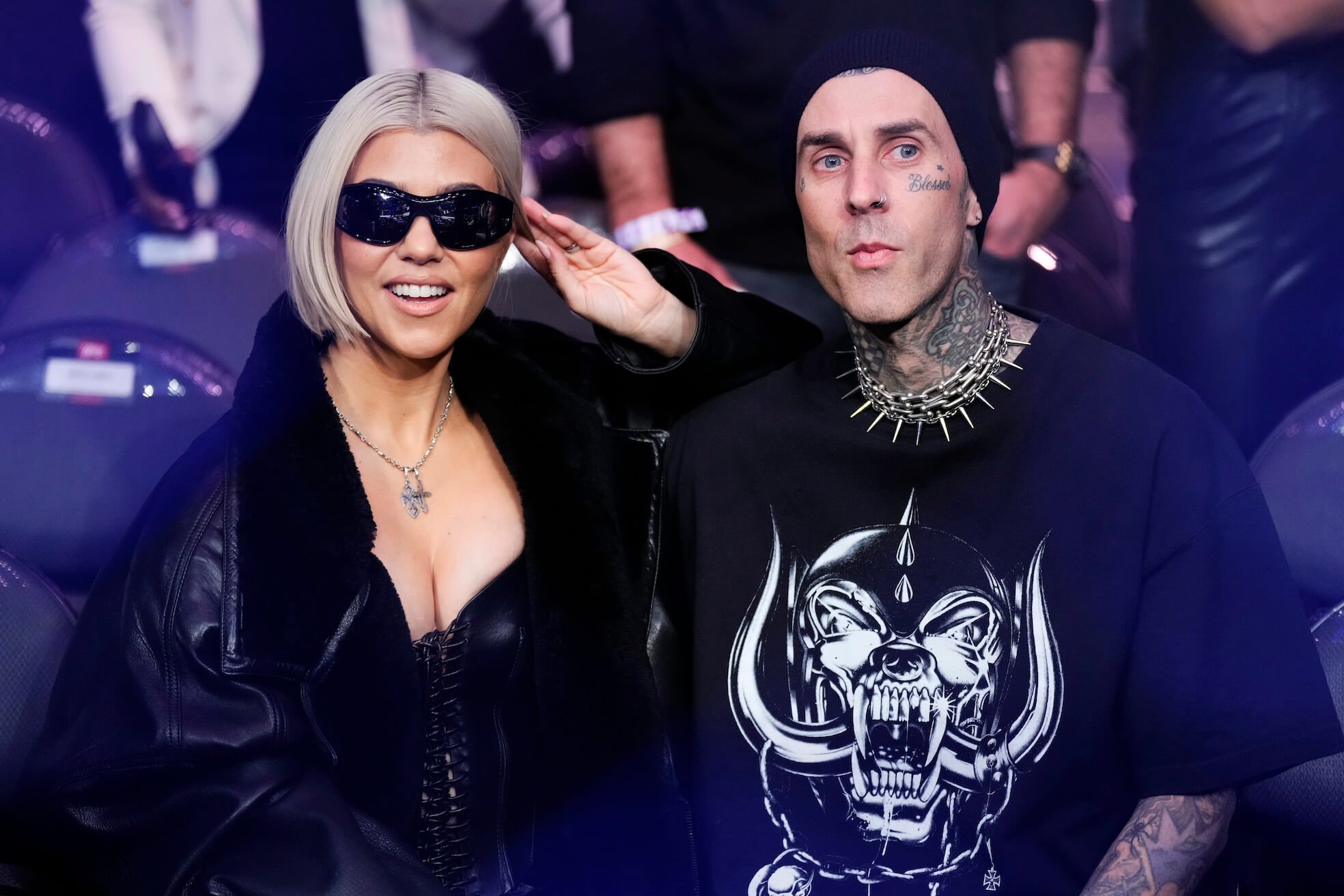 Kourtney Kardashian wearing sunglasses and smiling while sitting next to Travis Barker