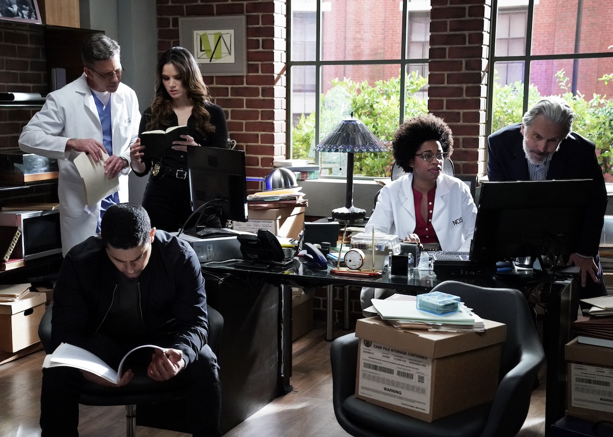 Members of the 'NCIS' team in an office looking through files and boxes