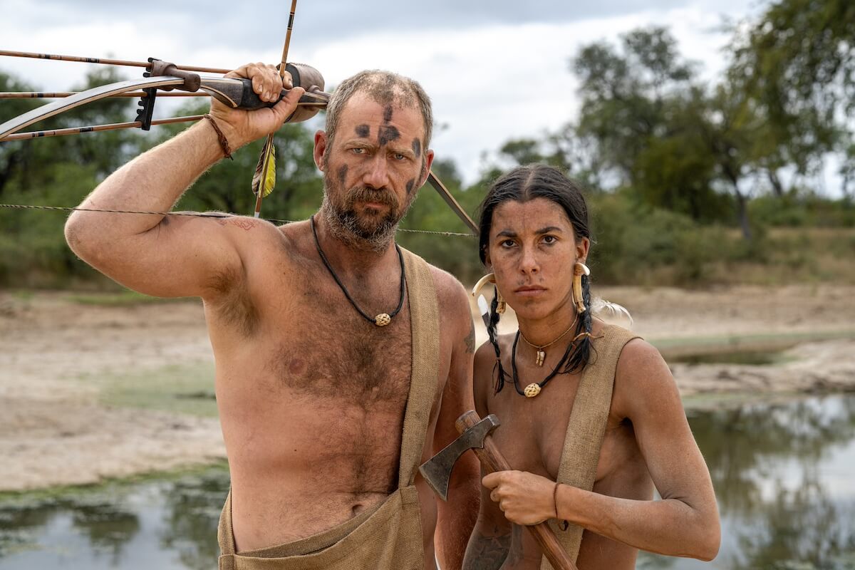 Coe, holding his bow and arrow above his shoulder, standing next to Michelle in 'Naked and Afraid'
