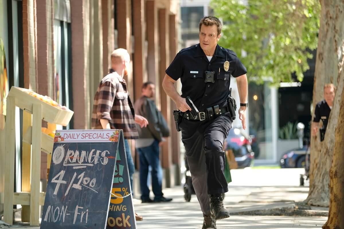 Nathan Fillion walking down the street while portraying the character John Nolan in 'The Rookie'.
