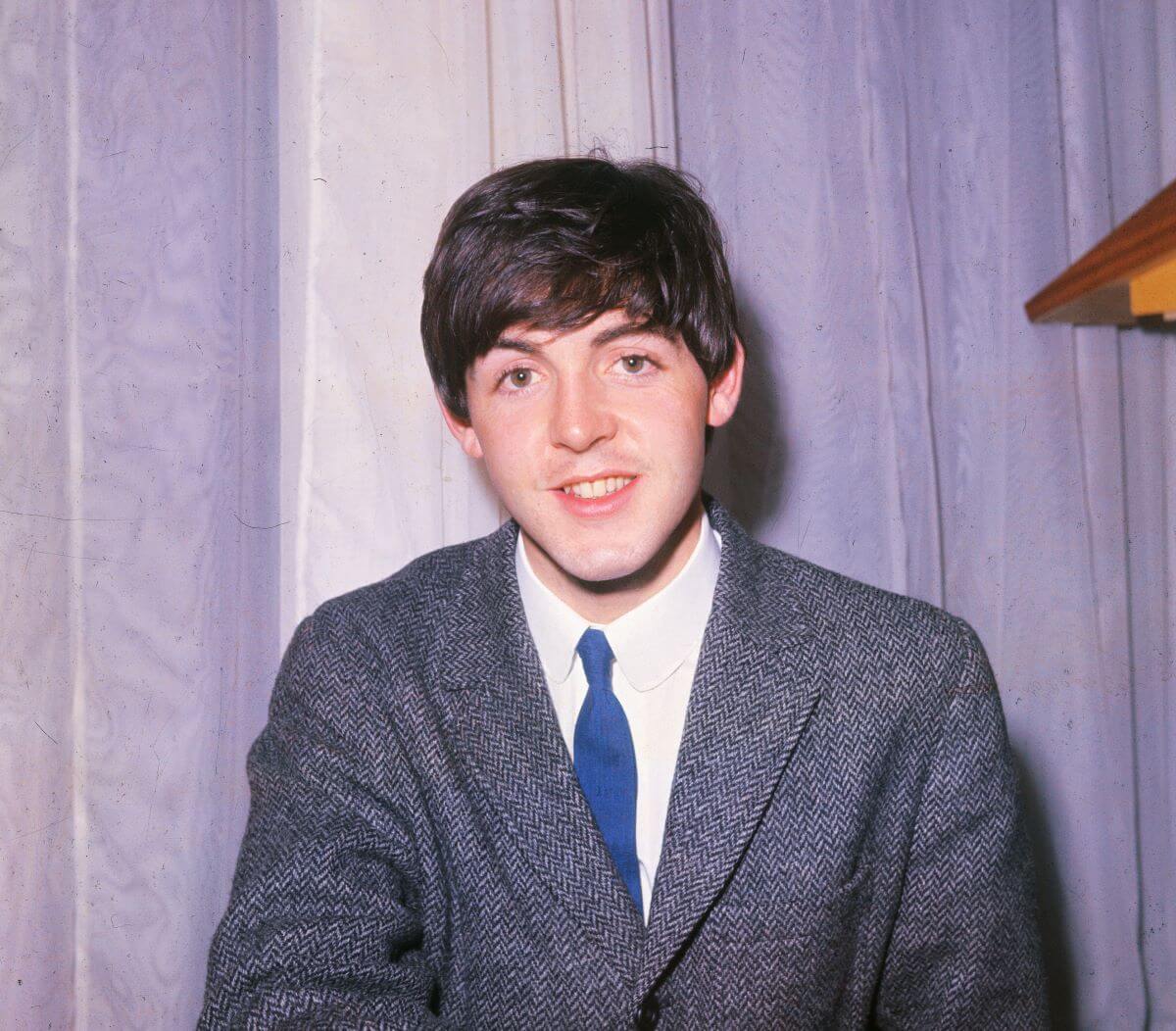 The Beatles' Paul McCartney wears a tweed jacket and sits in front of a curtain.
