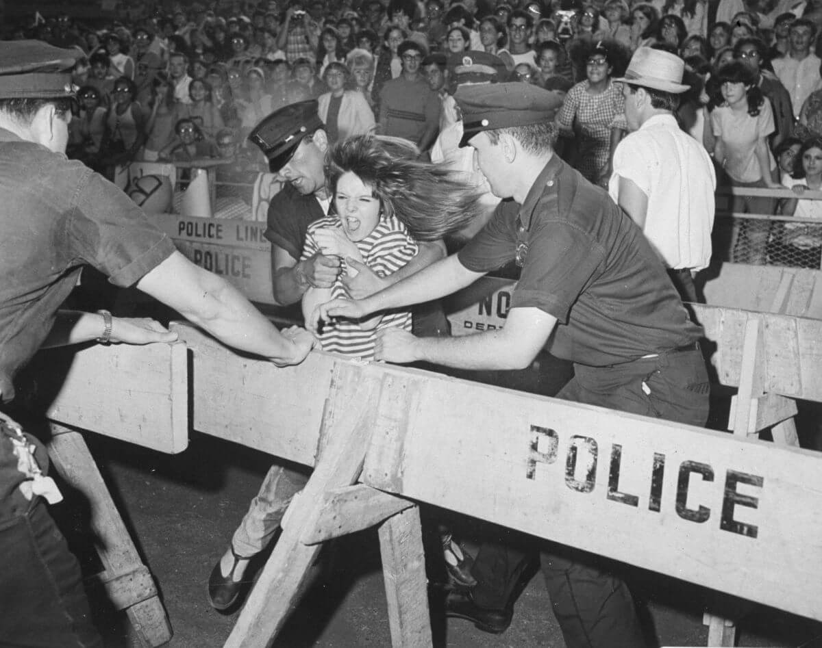 A black and white picture of police officers trying to stop a Beatles fan from behind a barricade.