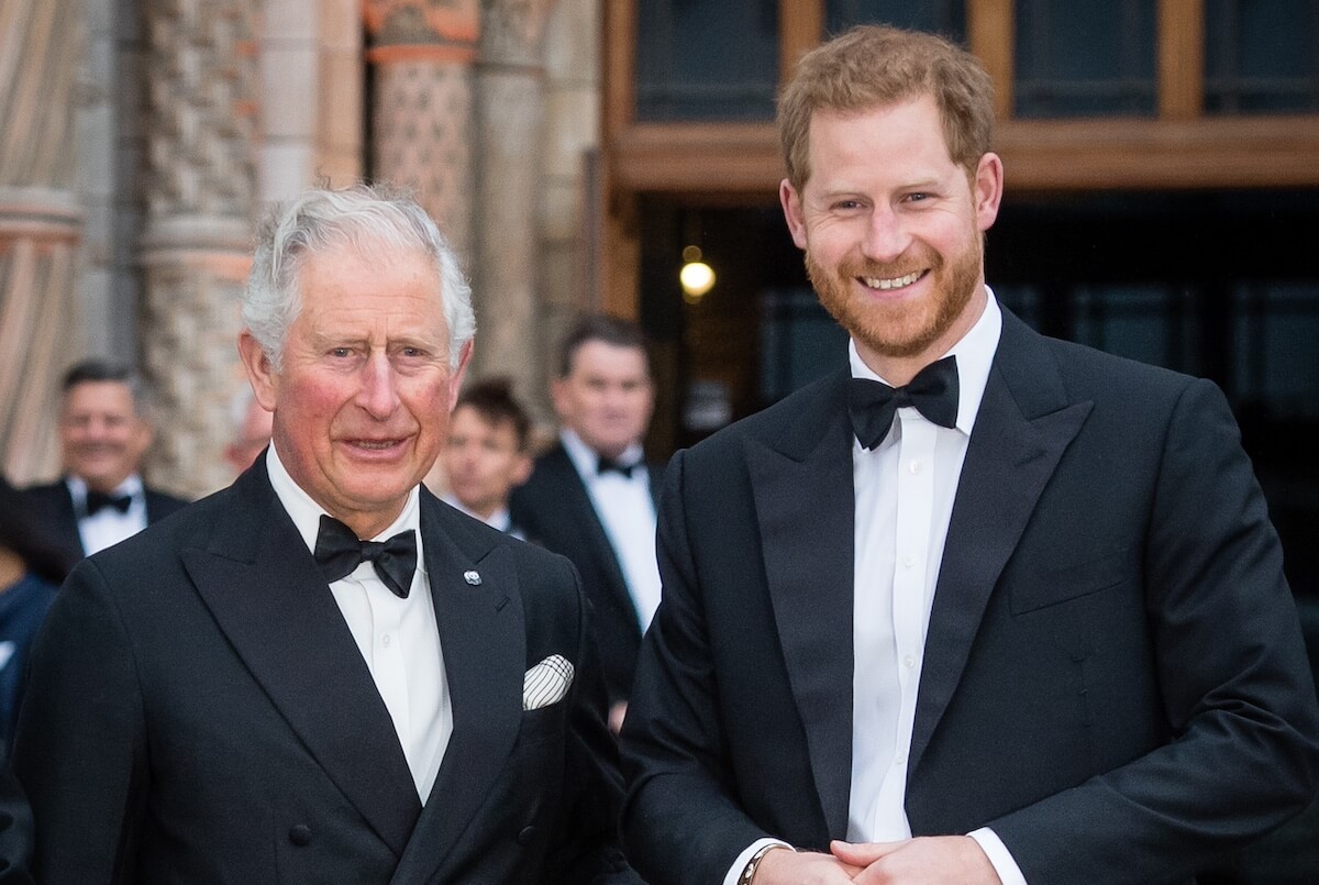King Charles and Prince Harry standing side-by-side and wearing tuxedos. 