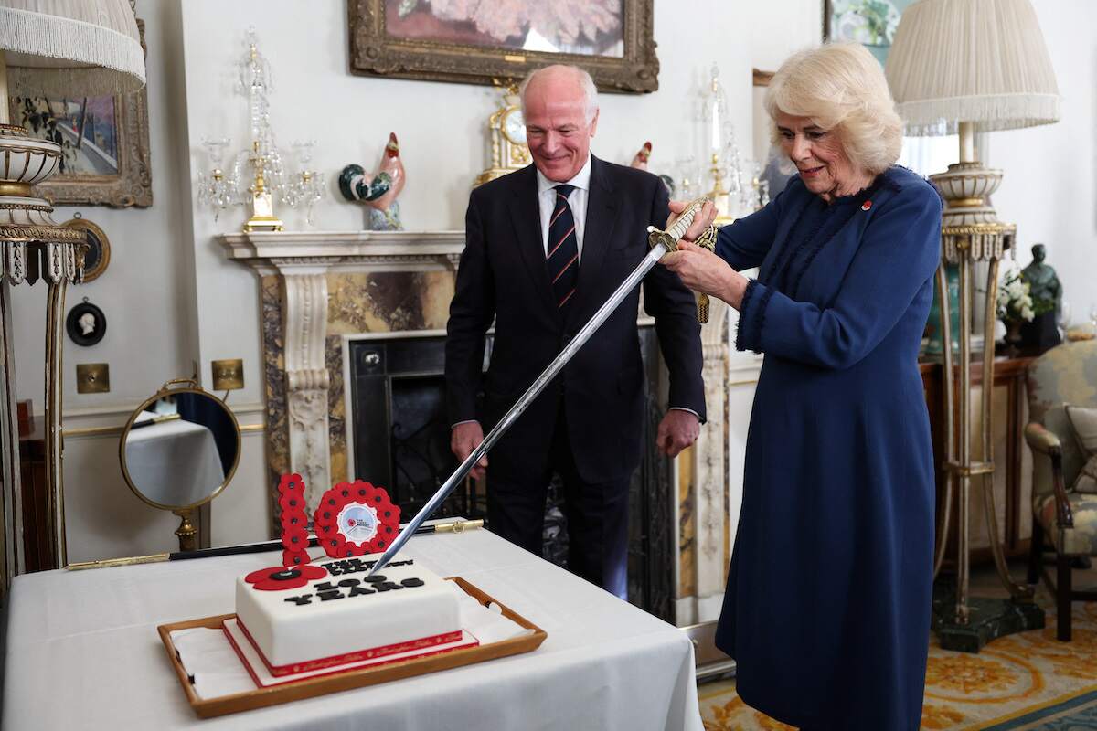 President of The Poppy Factory Surgeon Rear Admiral Lionel Jarvis helps Britain's Queen Camilla to slice a cake with a sword