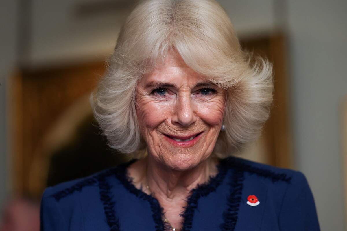 Camilla Parker Bowles wears a navy jacket while smiling for the camera at the celebration of The Poppy Factory Centenary