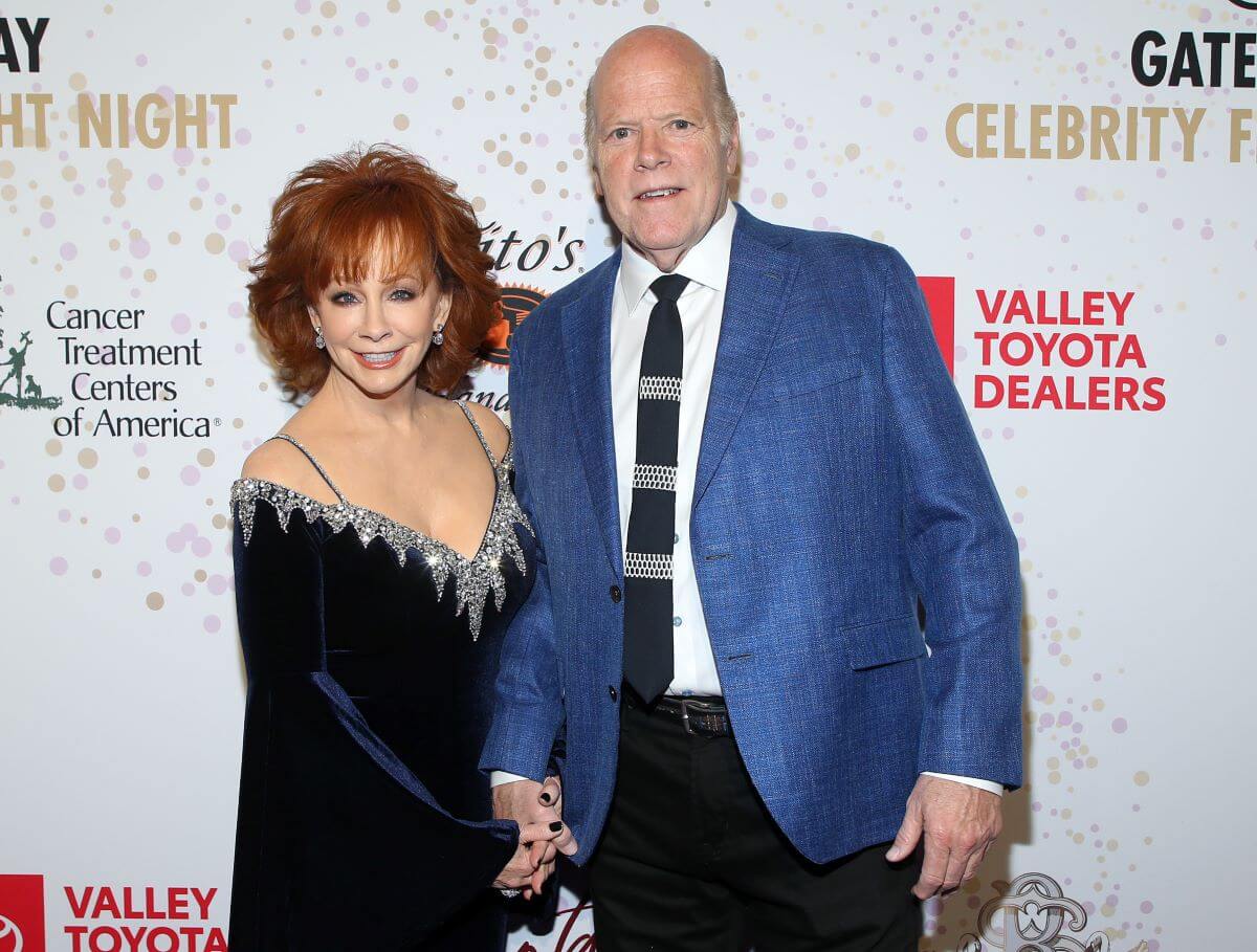 Reba McEntire wears a black dress and holds Rex Linn's hand. He wears a blue suit.