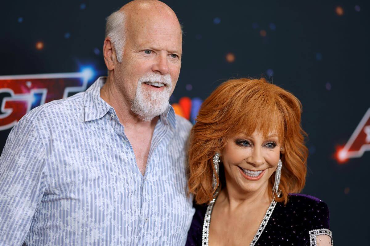 Rex Linn stands with his arm around Reba McEntire's shoulders. He wears a blue shirt and she wears black.