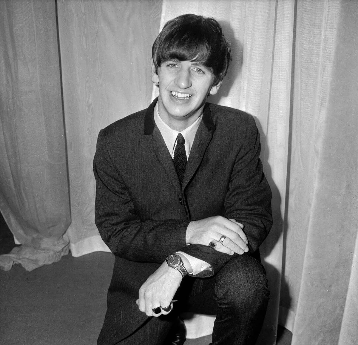 A black and white picture of Ringo Starr wearing a suit and kneeling.