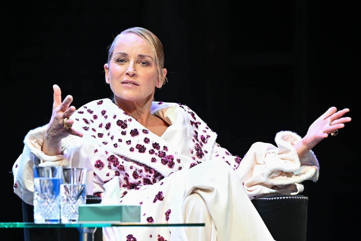 Actor Sharon Stone wears a white overcoat and sits onstage and speaks to the audience during a Q&A