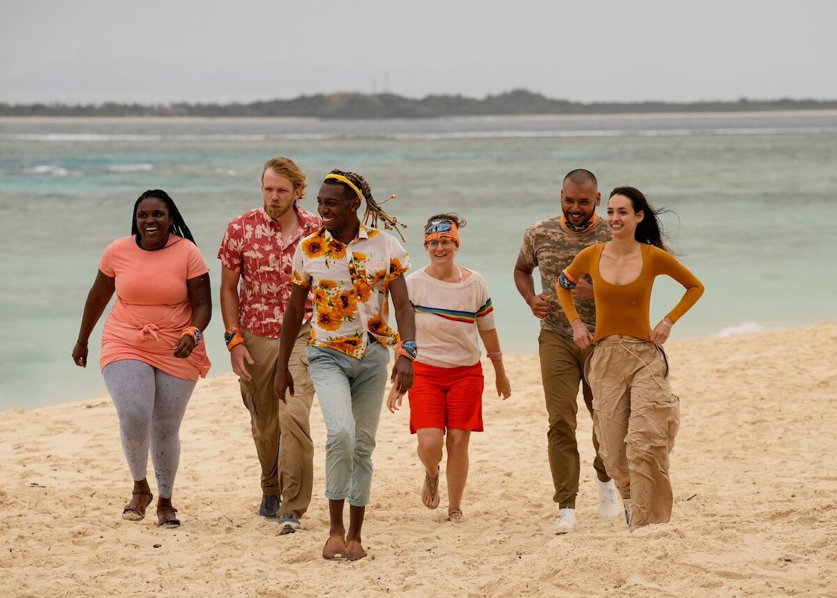 Six cast members from 'Survivor 46' standing in the sand on the beach