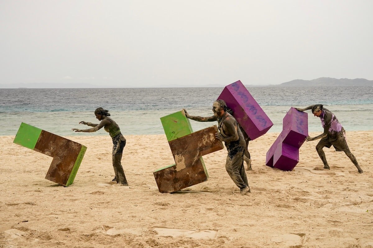 'Survivor 46' cast members rolling giant puzzle pieces in the sand