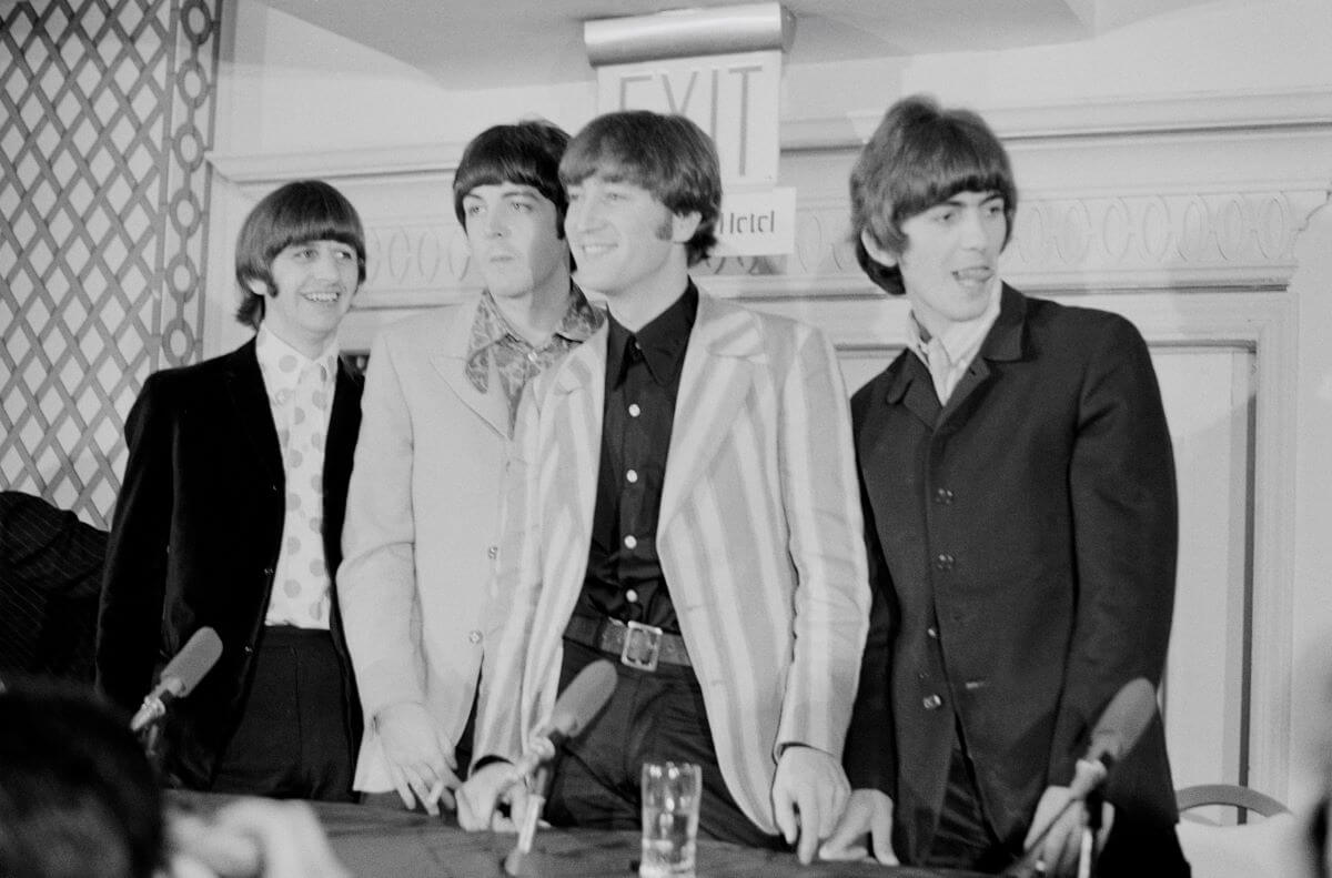 A black and white picture of The Beatles standing together behind a table.