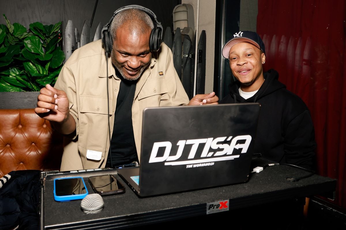 Tree wears headphones and leans over a laptop. He stands next to Dj Ditisa.