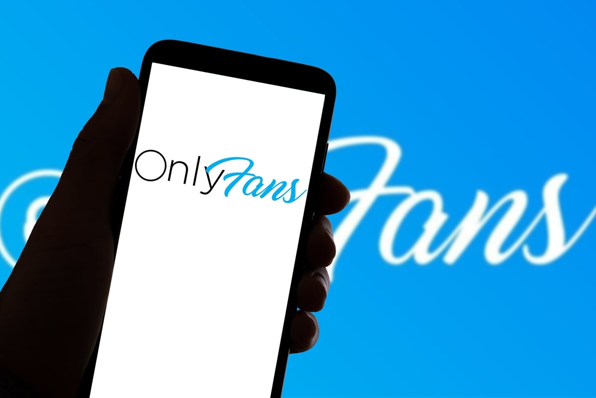 The Onlyfans app logo is seen on the screen of a mobile phone and on a laptop in the background